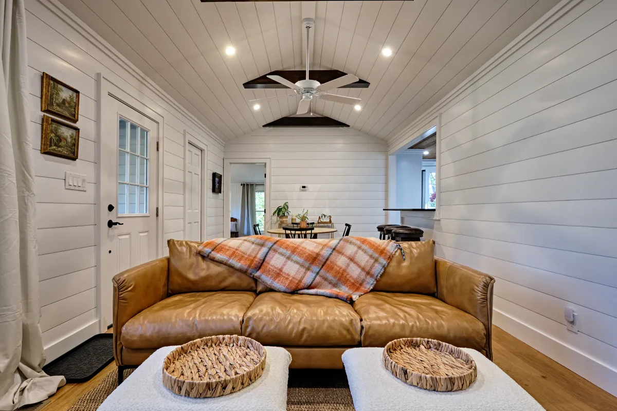 A spacious, inviting communal living area with a plush leather sofa draped in a plaid blanket, rustic wooden coffee tables, and vibrant art on the wall. The mood is casual and social, ideal for unwinding or gathering after outdoor excursions.