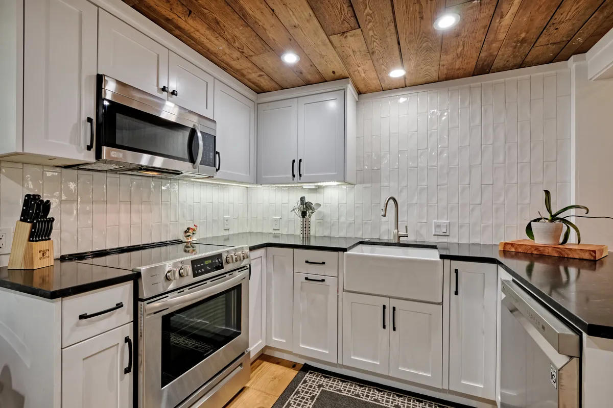 A closer angle focuses on the kitchen’s stainless steel appliances, a large farmhouse sink, sleek black countertops, and a visually interesting textured backsplash. The modern and functional design elements invite both everyday cooking and special culinary occasions.