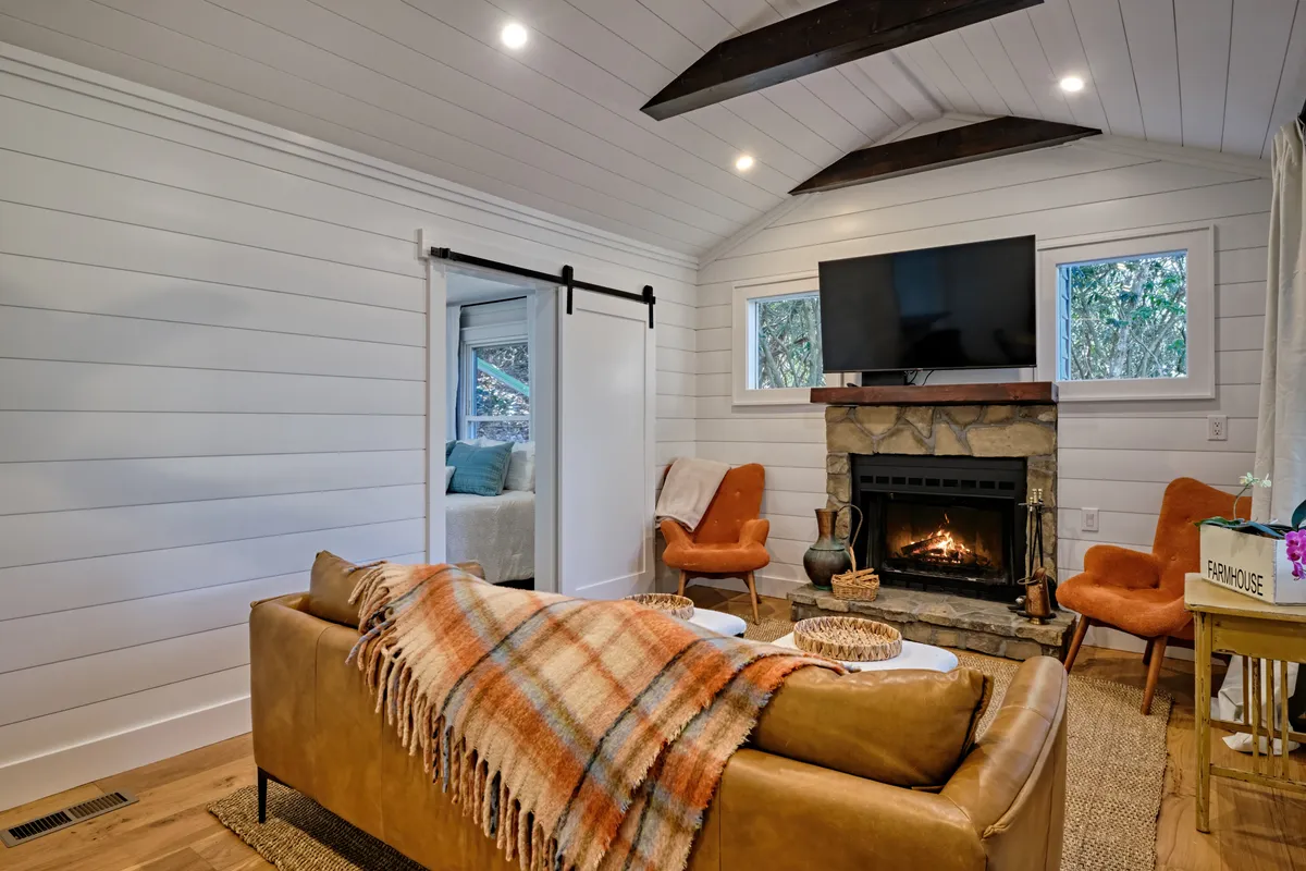 An open-plan living room is showcased, with a sofa facing a television, fireplace (not in use), and large windows letting in ample natural light. Decorative accents and the arrangement of furniture foster a sense of togetherness and comfort, ideal for game nights or group gatherings.