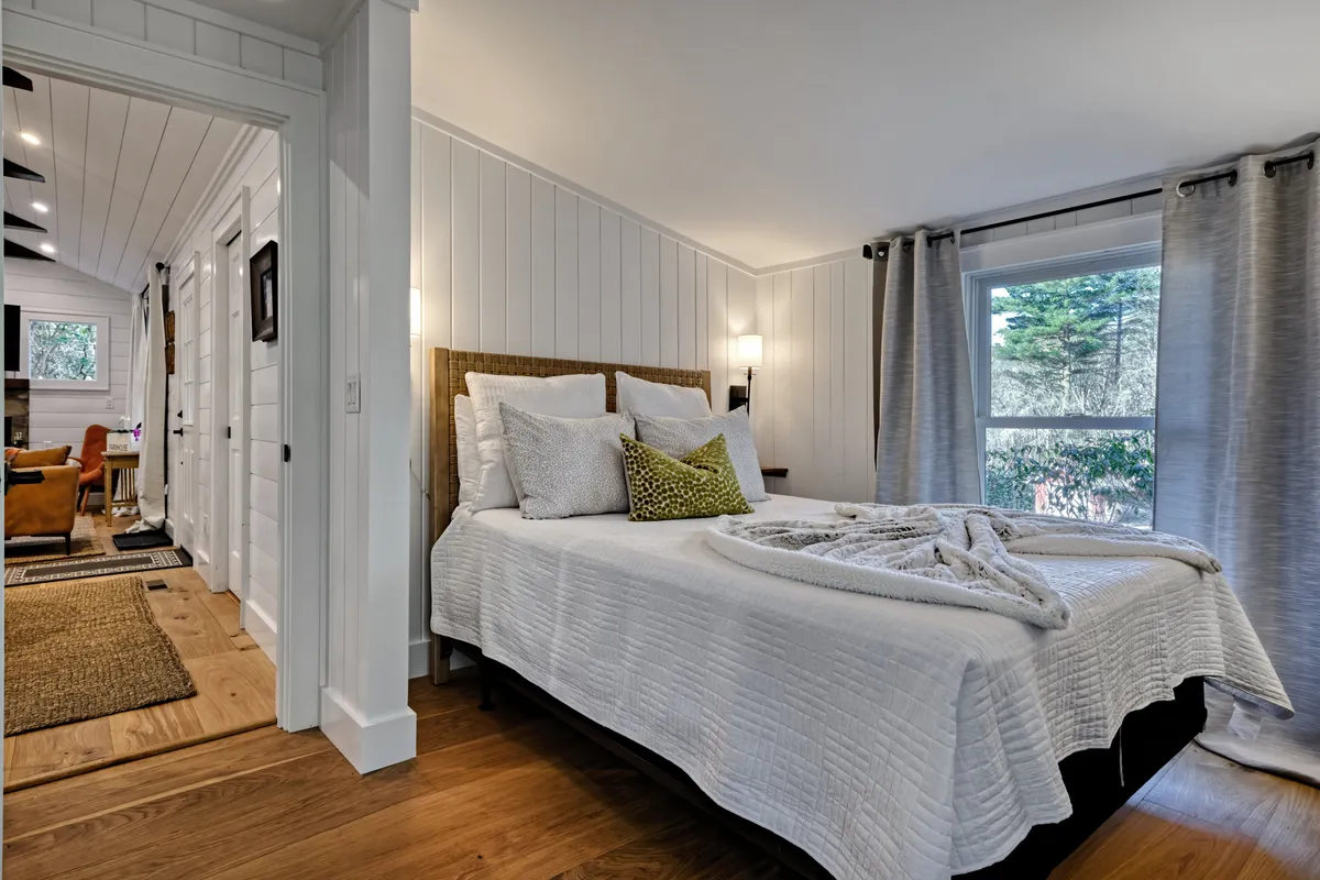 A serene bedroom featuring a queen bed with decorative pillows, a textured blanket, and a window that allows natural light to fill the space. The overall atmosphere is calm and restful, perfect for unwinding after a day of outdoor activities.